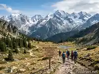 Международен ден на планината: Група туристи по планинска пътека сред величествени върхове и езеро.